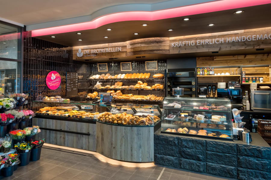 Kempten Baeckerei Schwarz Bäckereitheke im Supermarkt mit Broten, Gebäck und Blumen im Eingangsbereich.